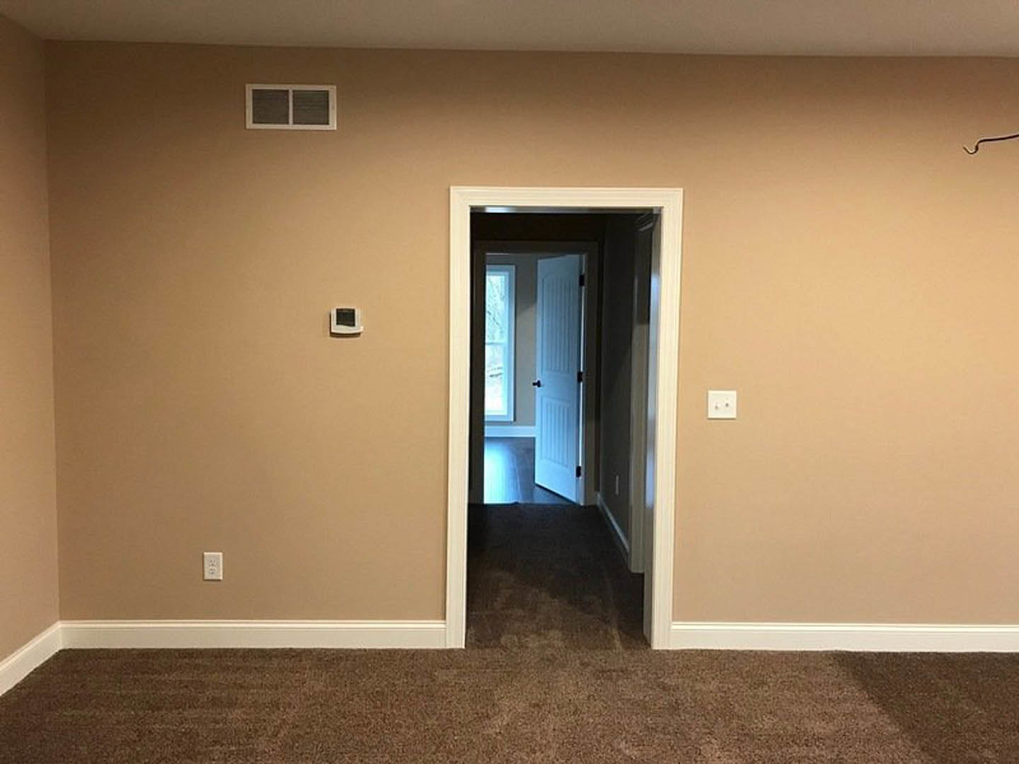 White paneled door open in carpeted hallway, white light switch and thermostat on plaster wall