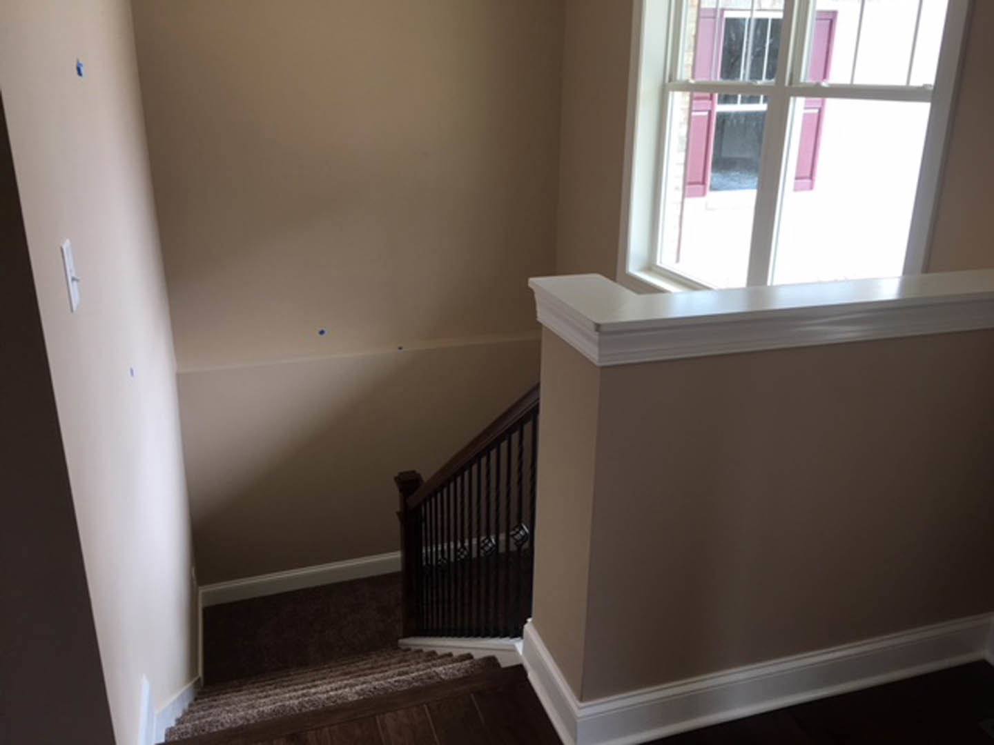 Carpeted staircase with white trim, adjacent window with white frame, built-in white shelf, and plaster walls in a residential interior.