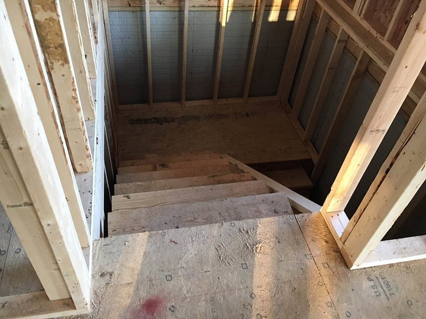 Wooden staircase with open risers, natural wood beams along the wall, light fixture on the floor, hardwood plank flooring, and neutral-toned walls in a modern interior.