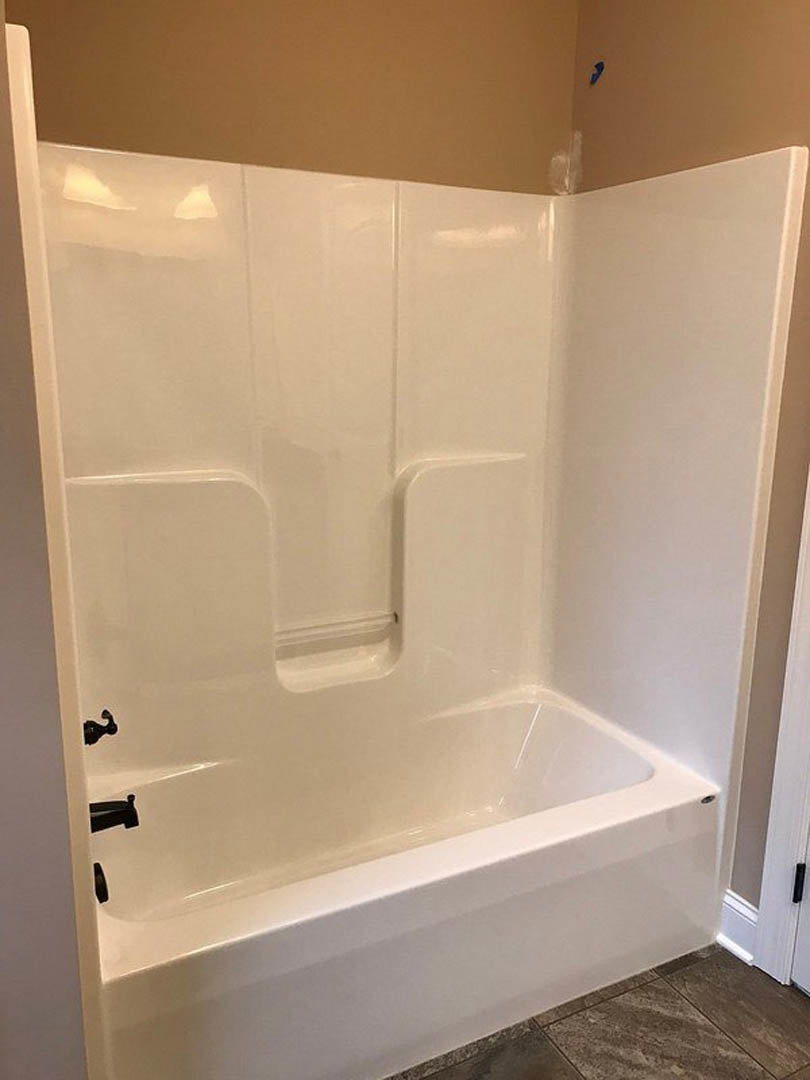 Freestanding white bathtub with black faucet on marble tile floor, white walls, and open glass shower door in modern bathroom