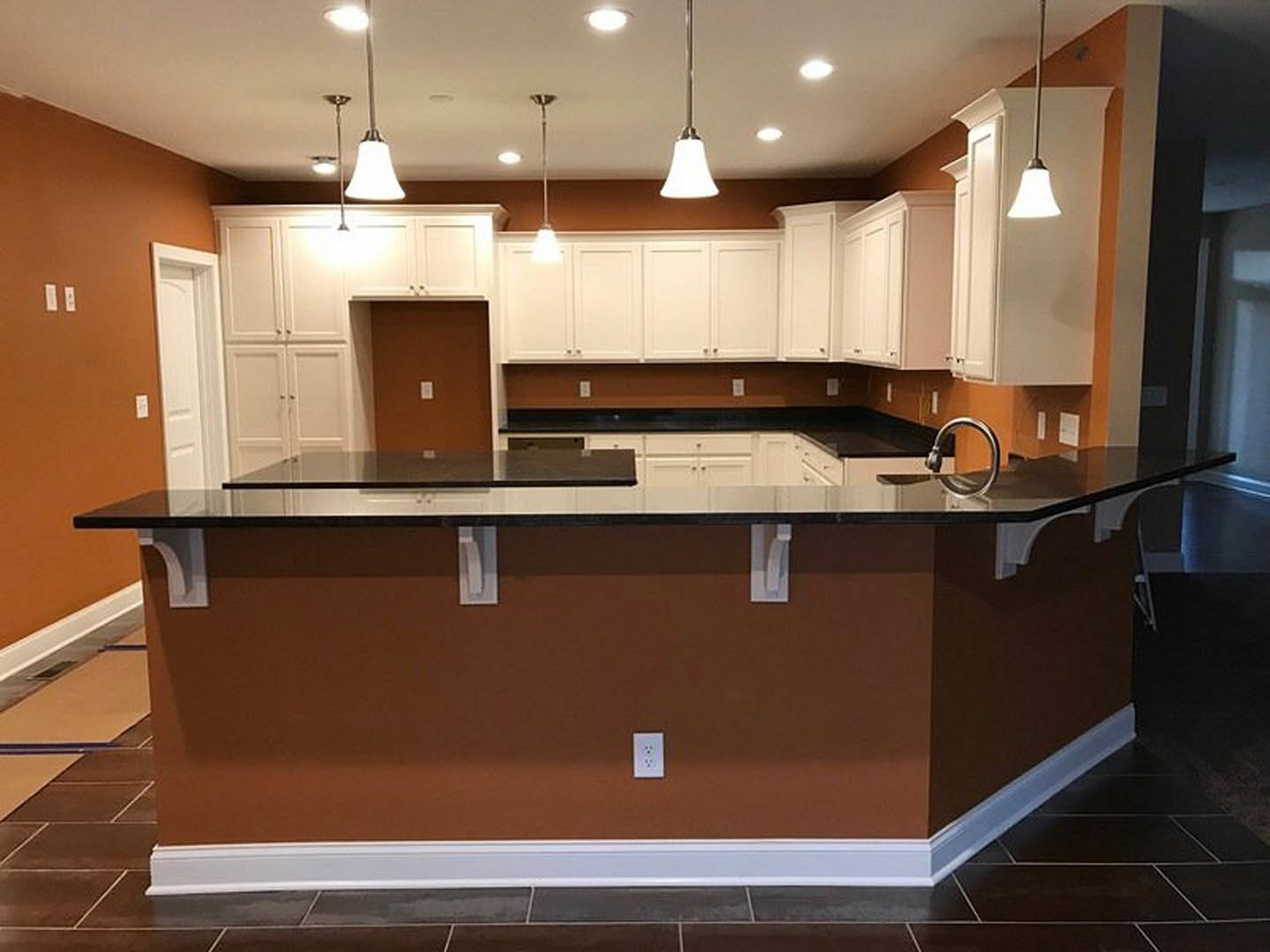 Modern kitchen with black countertop, white cabinetry, built-in sink with chrome faucet, bar seating, and white appliances; wall outlets visible near backsplash, light wood