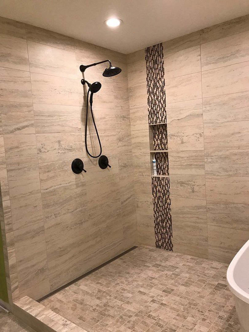 White freestanding bathtub beside glass-enclosed shower with chrome shower head, gray tiled floor, and recessed ceiling light