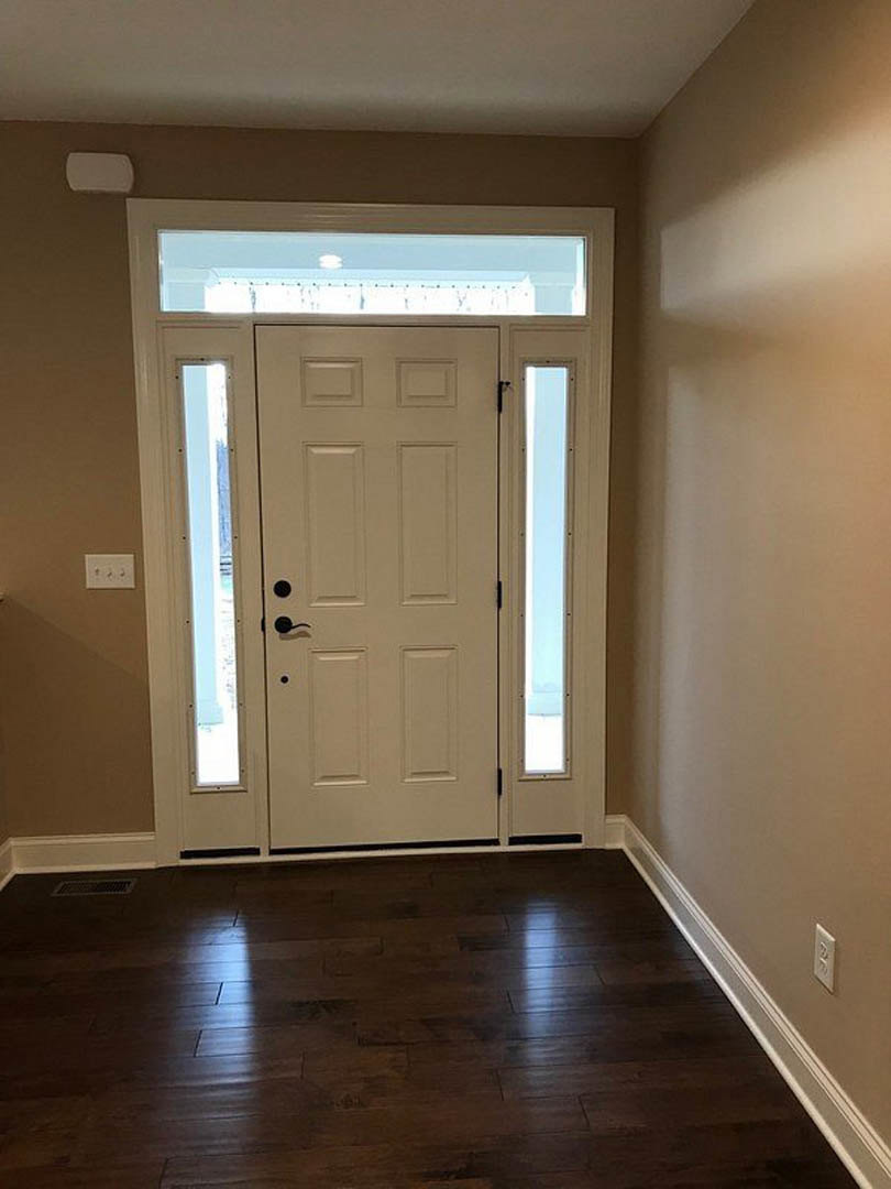 White paneled door with glass windows, brushed metal handle, set in a light-colored wall above dark wood flooring