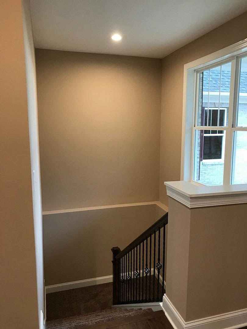 White-painted staircase with black metal railing, adjacent to a large window and white walls, light wood flooring, and a bright, airy interior.