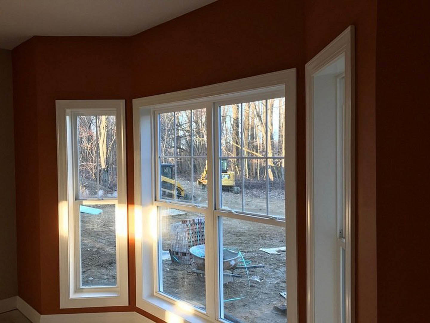 Unfinished room with large windows overlooking active construction site, yellow truck and caution sign visible outside, white walls and ceiling inside