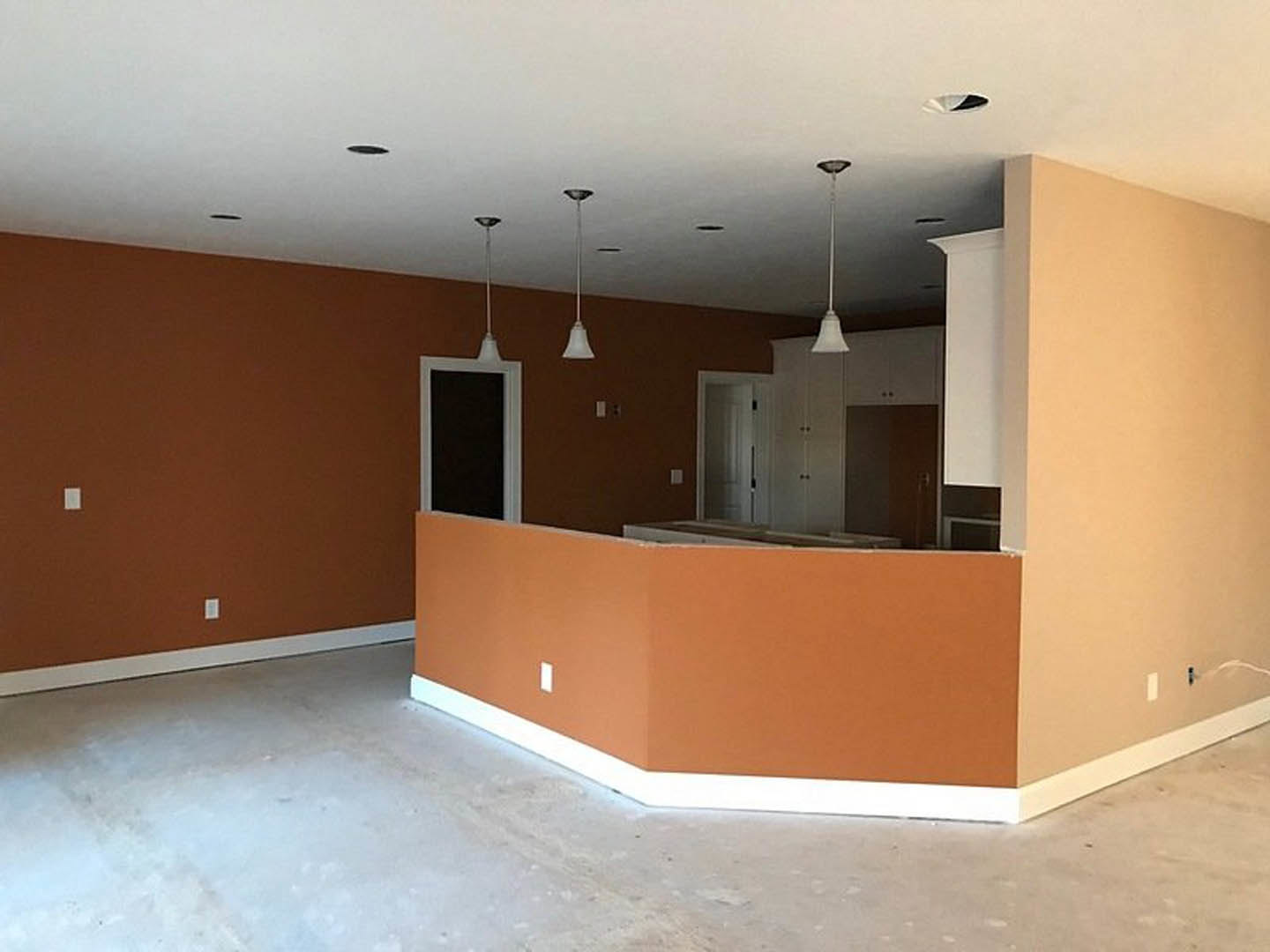 Open kitchen and dining area with orange walls, white ceiling, light wood flooring, white door with black handle, black rectangular appliance with white frame, and white poles with