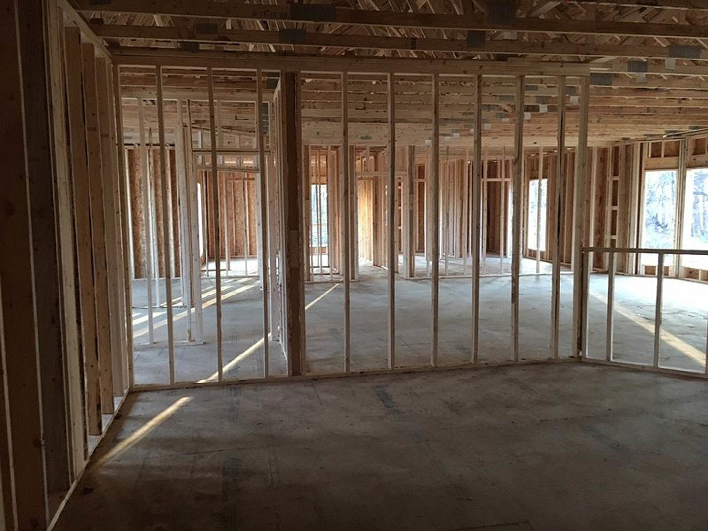 Wood-framed room under construction with exposed beams, concrete floor, and large windows letting in daylight