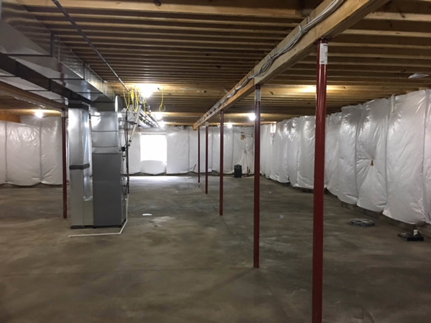 White-walled room with exposed wooden ceiling beam, metal poles, and rows of white plastic bags on the floor; red post stands near a white background.