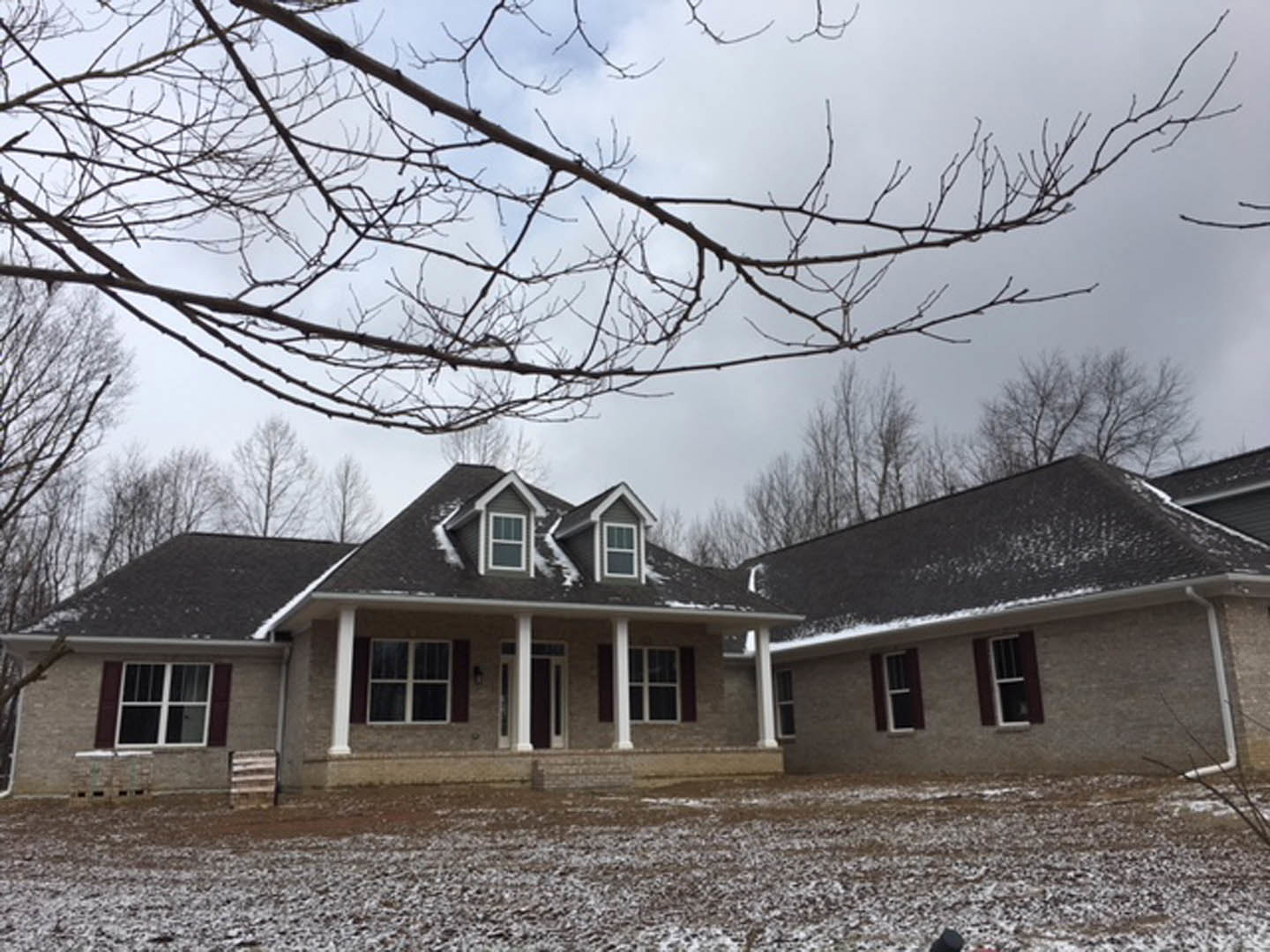 Two-story house with white-framed windows, snow-covered roof and ground, leafless tree branches, and wooden front door