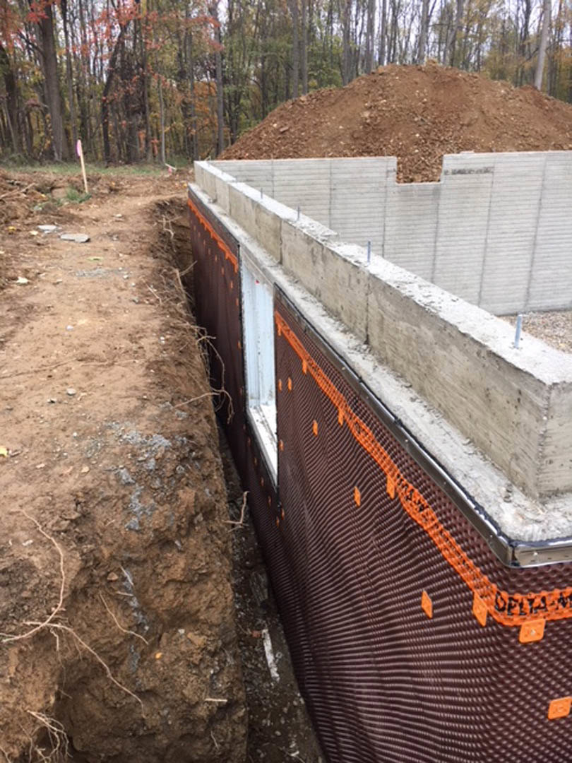 Concrete foundation slab surrounded by dirt and wood chips, bordered by forest trees in the background