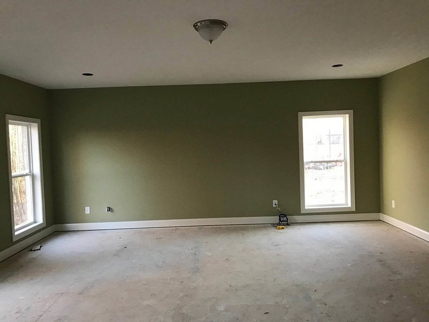 Green-painted walls, white-framed window, concrete flooring, ceiling-mounted light fixture