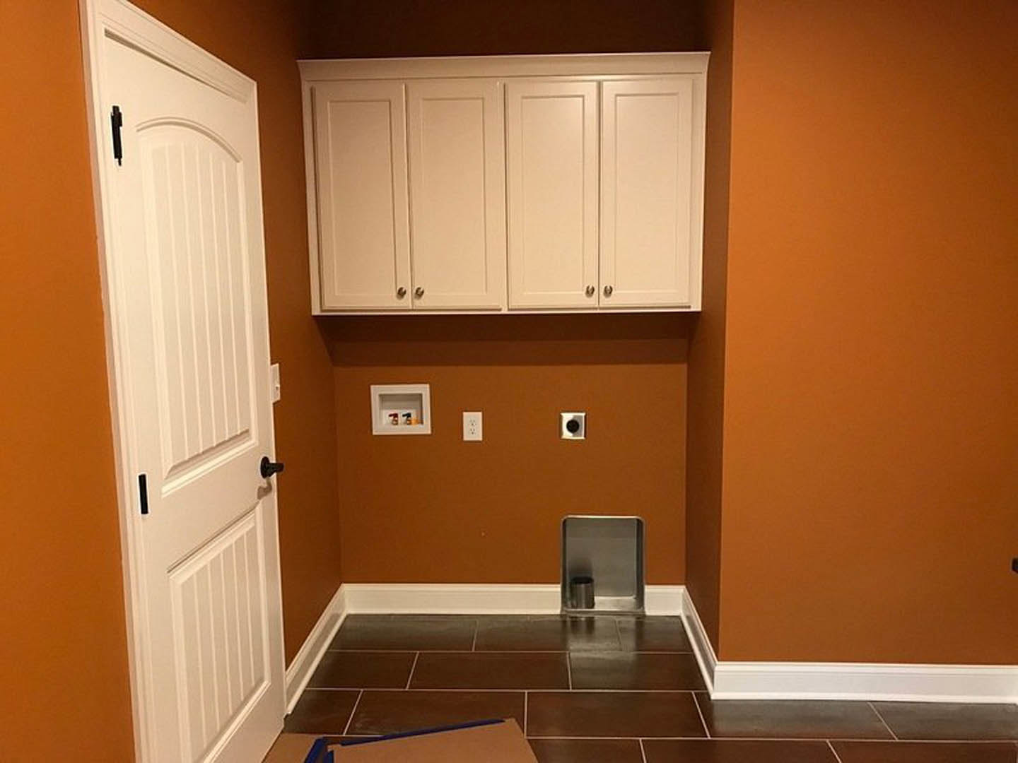 Kitchen with vibrant orange walls, white cabinetry, metal container on open shelf, white square shelf with black circular accent, light wood countertop, and modern appliances