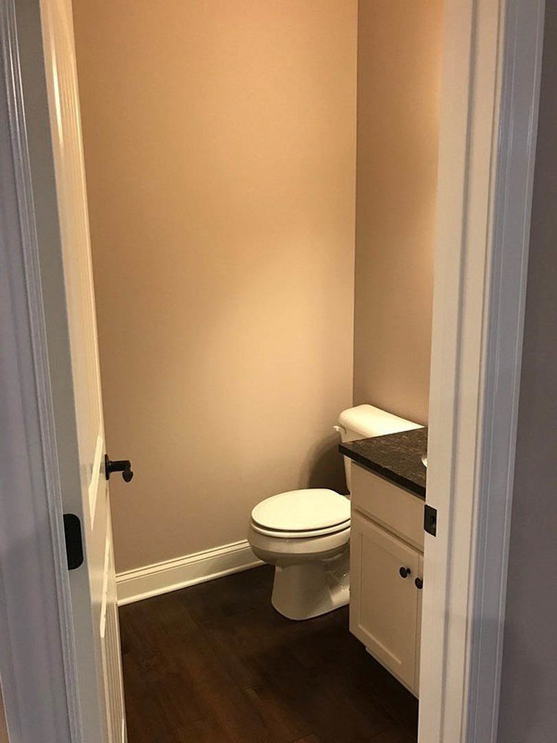 White toilet with closed seat beside rectangular sink on stone countertop, light tile walls, wooden floor, chrome fixtures