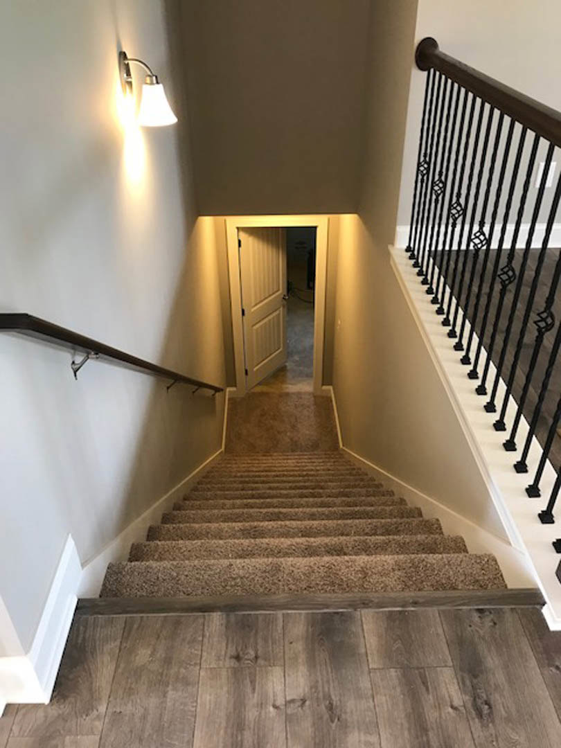 Carpeted staircase with wooden handrail and balusters, wood flooring at the base, open doorway leading to a room, plaster walls and ceiling