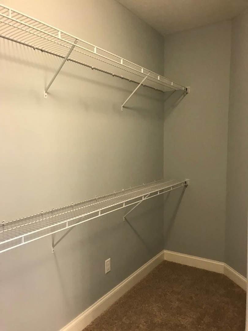 Walk-in closet with white built-in shelves and metal hanging rods, brown carpet flooring, white plaster walls, and ceiling