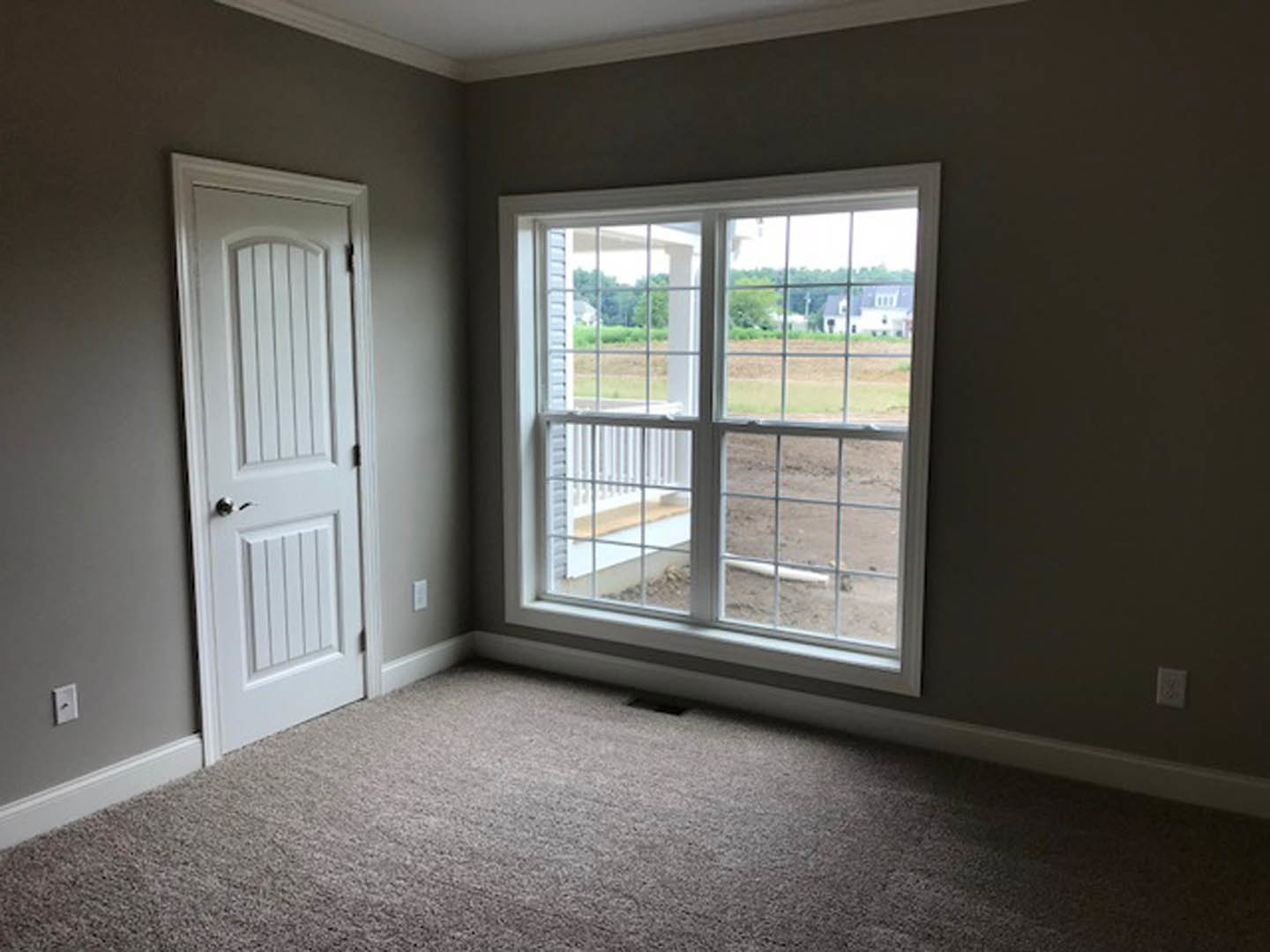 Carpeted floor in a residential room with a large window, white walls, window blinds, and a white electrical outlet.