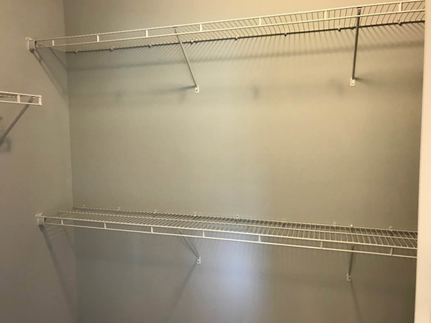 White metal shelves mounted on a white wall in a bathroom closet, with indoor lighting and minimal decor.
