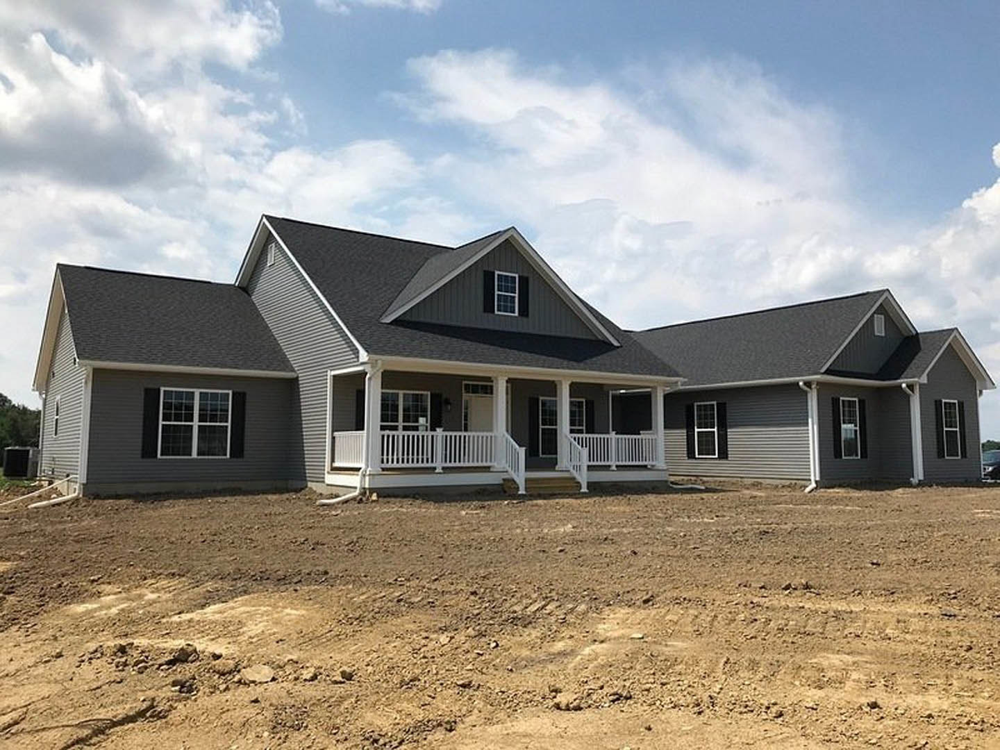 Partially built house with white porch railing, grid windows, and dirt yard under cloudy sky