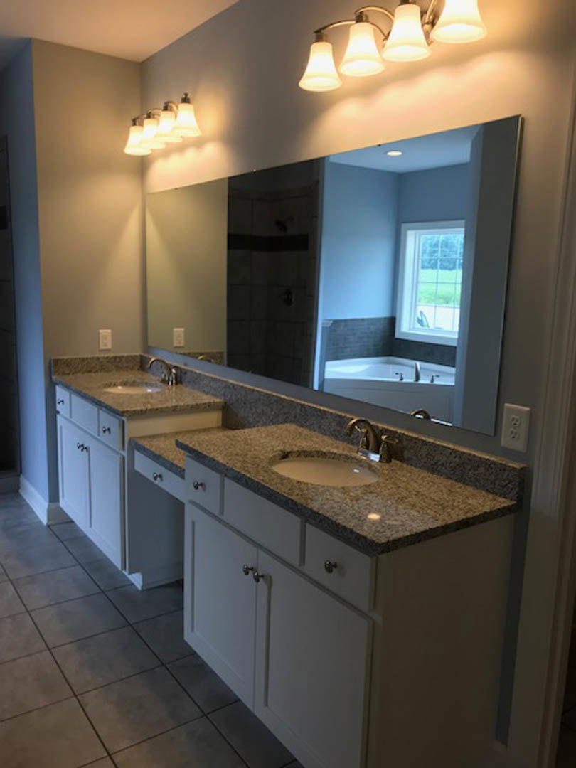 Bathroom with expansive mirror above white countertop, light fixtures mounted on wall, tile flooring, and white cabinetry.