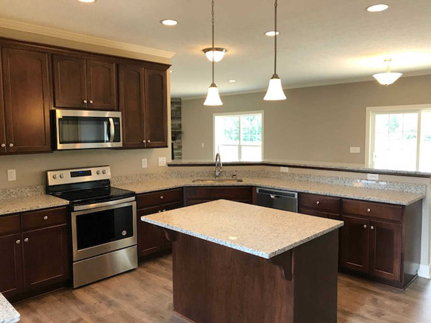 Granite countertops, stainless steel stove and oven, white cabinetry, overhead pendant lights, built-in microwave, neutral wall color