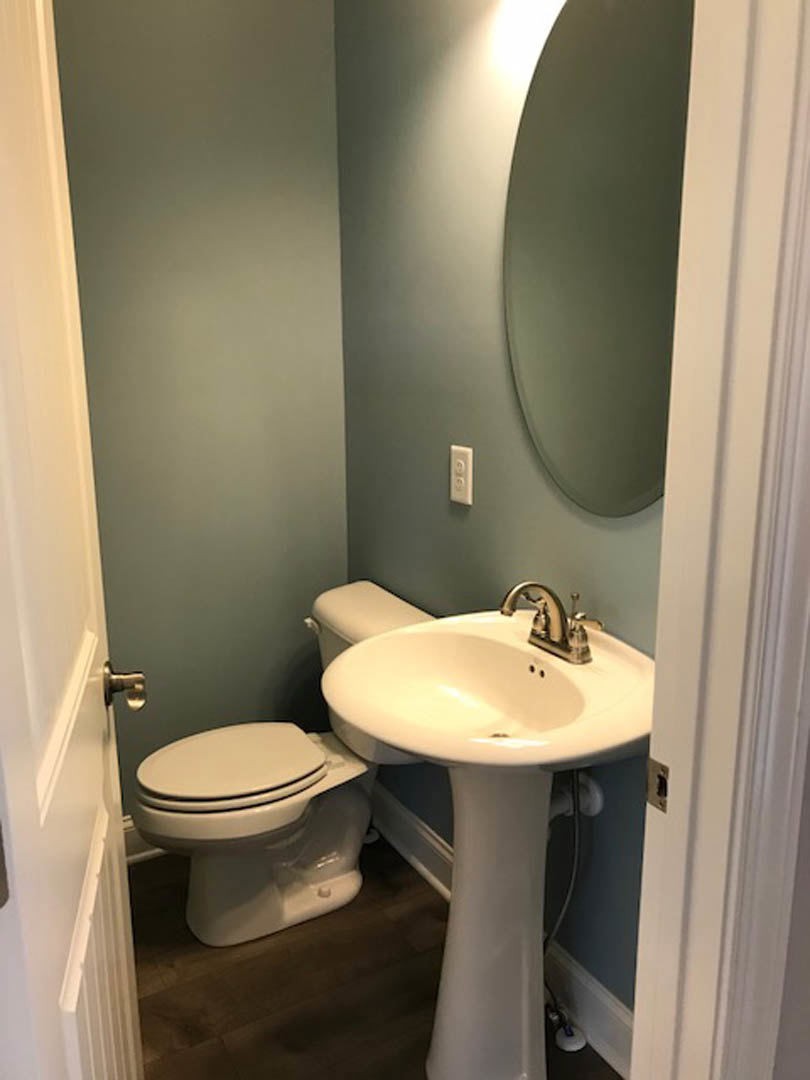 Bathroom with round wall mirror above white sink, chrome faucet, and toilet; light tile walls and minimal decor.
