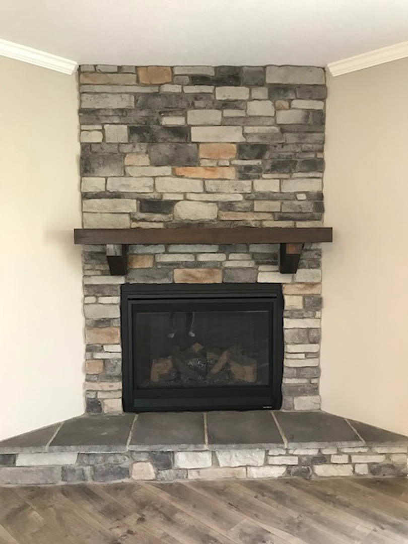 Stone fireplace with glass door, wood mantel shelf, wood flooring, and partial view of a person's leg in foreground