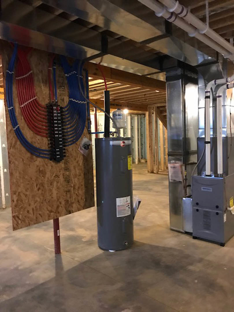 Large grey waste container with a white lid positioned indoors near red and blue pipes on a concrete floor.
