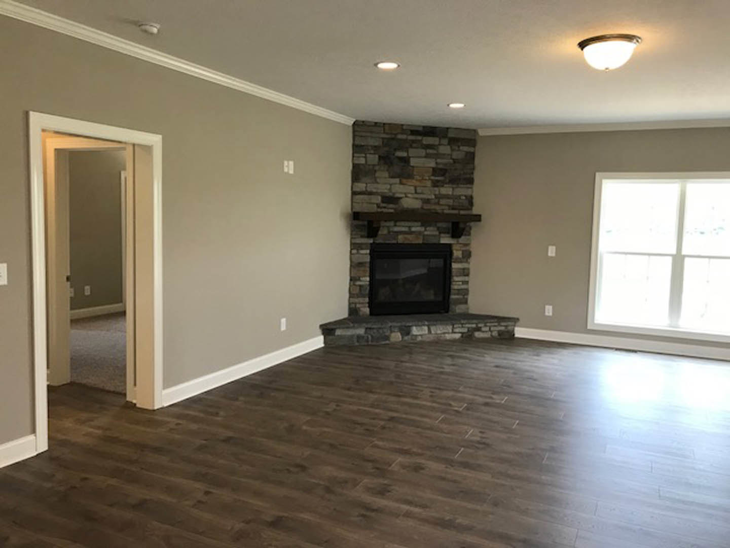 Living room with stone fireplace, hardwood floors, white walls, large windows, and recessed lighting