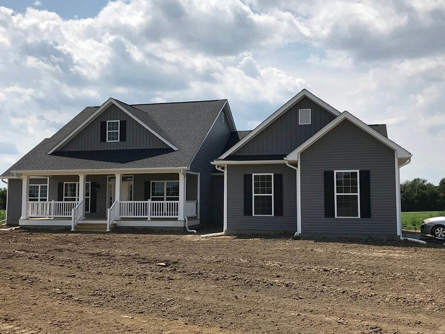 Two-story house with white porch railing, white-framed windows, and a dirt field in the foreground under a cloudy sky.
