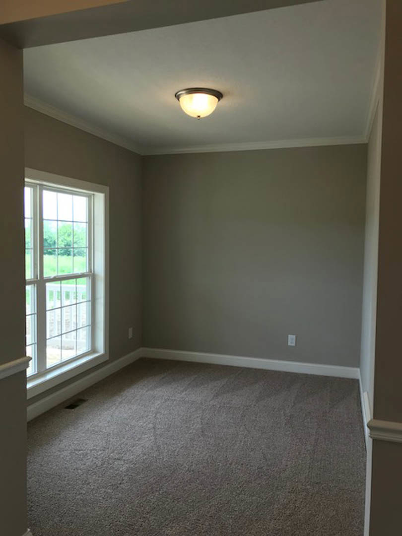 Carpeted room with white walls, round ceiling light fixture, large window overlooking grassy yard