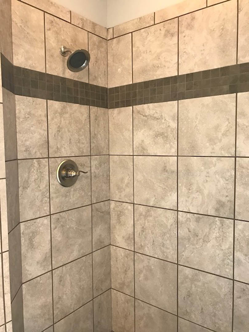 Walk-in shower with marble tile walls, chrome shower head, and matching tile flooring