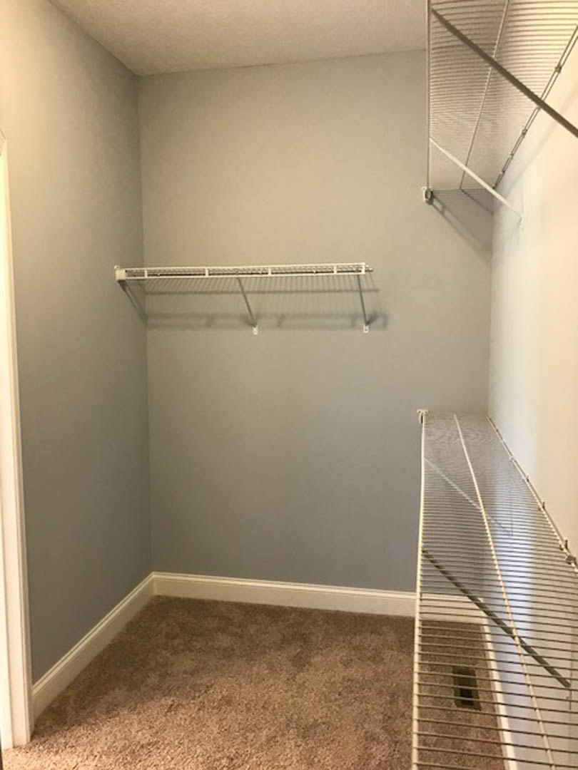 Walk-in closet featuring built-in white shelves, carpeted floor, and a white metal staircase with matching railing; close-up views of shelving, metal hanging rod, and stair grate