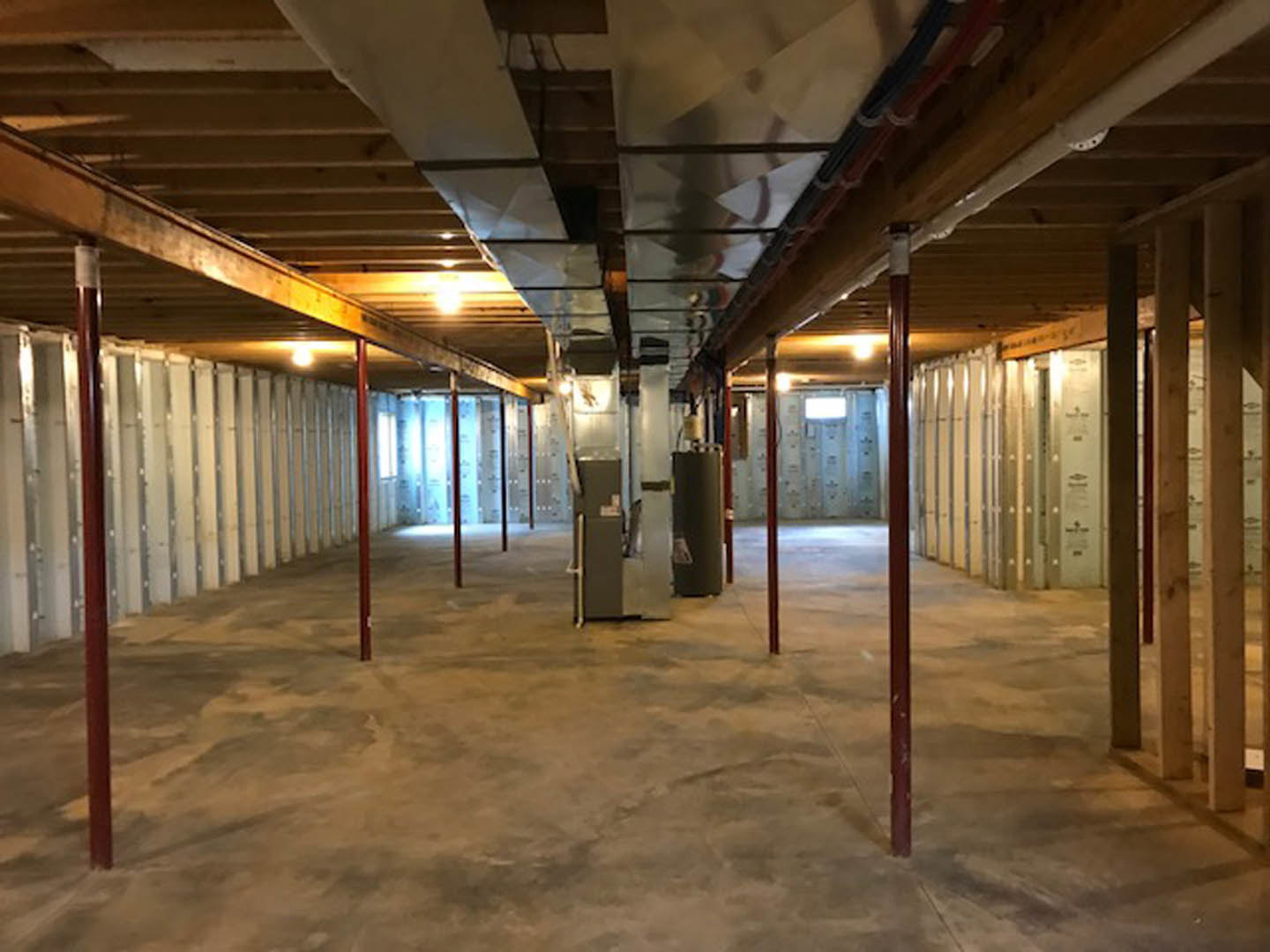 Concrete floor with refrigerator, exposed metal beams and poles, metal wall panels, bright overhead lighting, close-up of wooden post