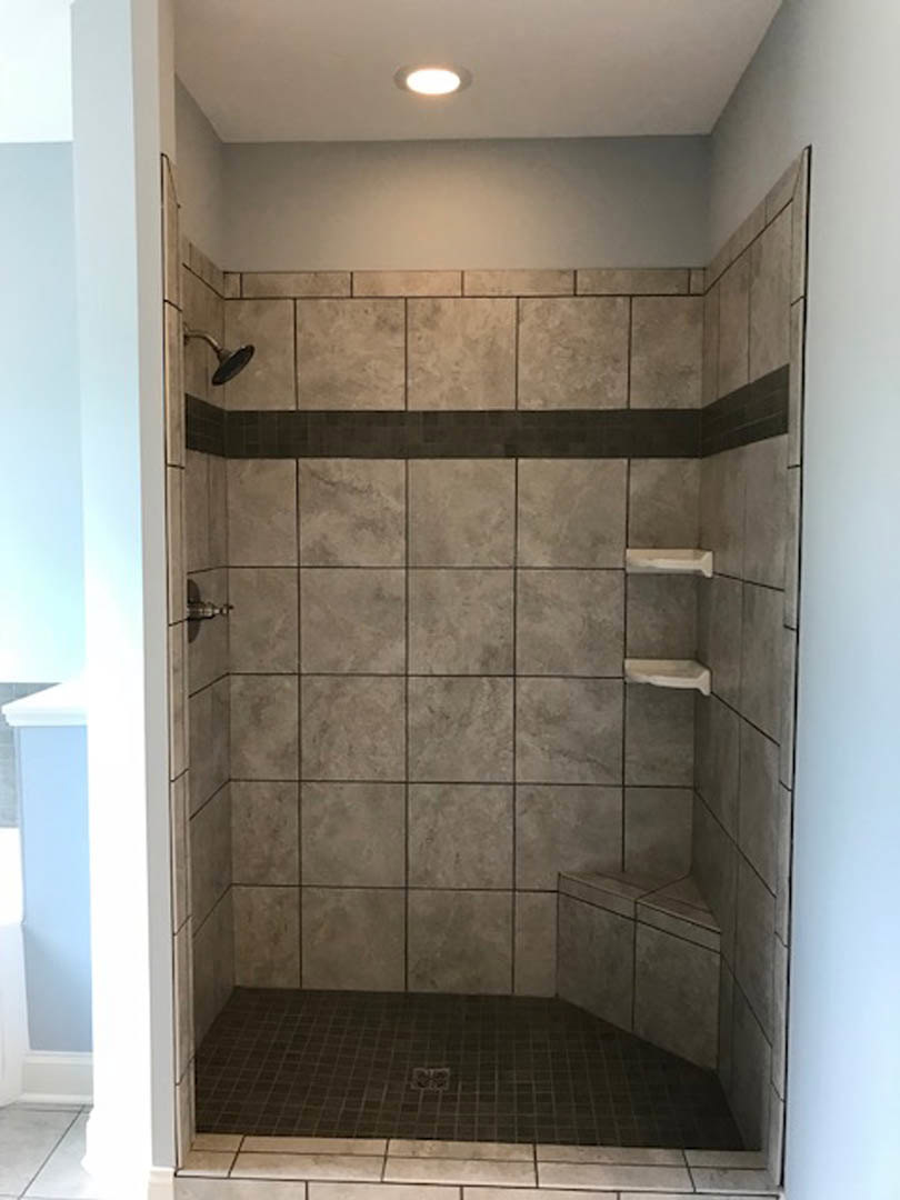 Walk-in shower with wall-mounted shower head, built-in shelves, light-colored tile walls, and tile floor with central drain