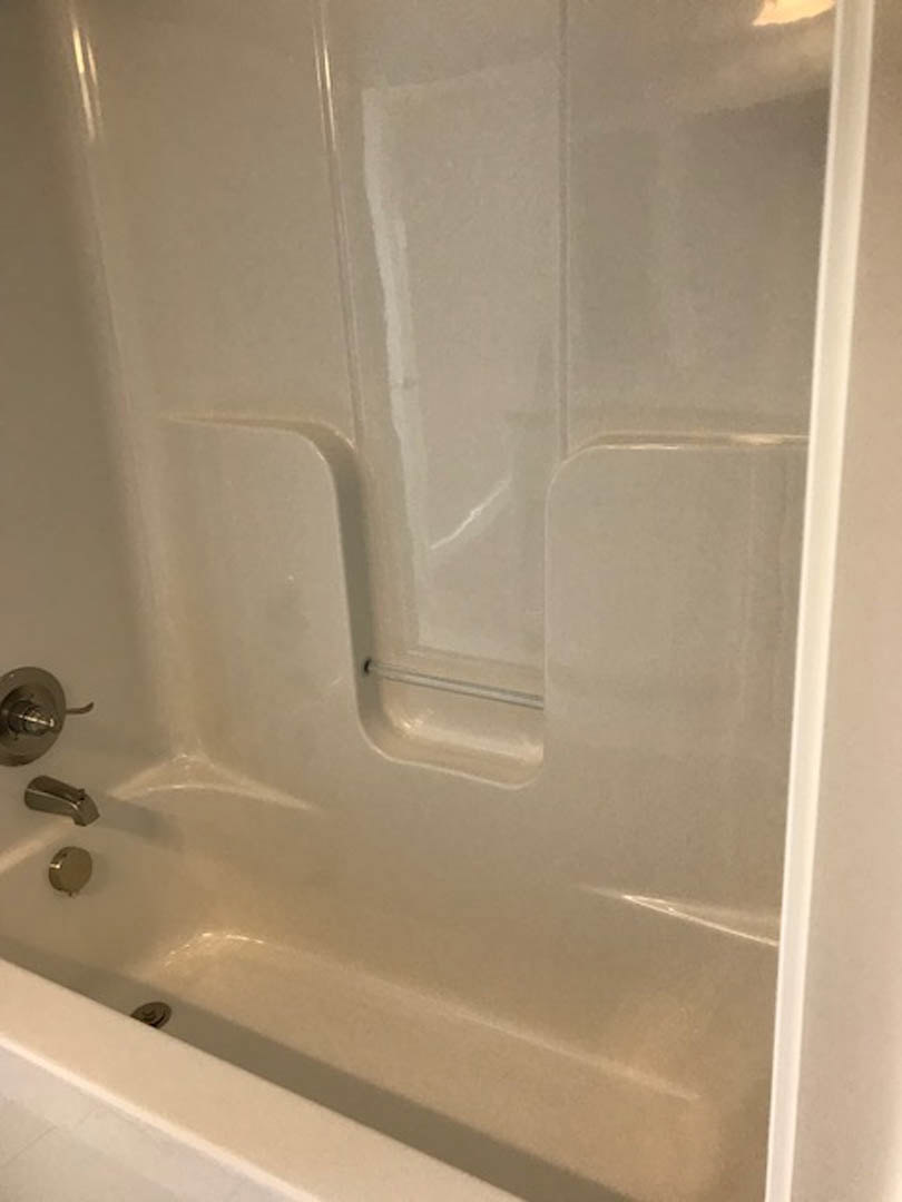 White bathtub with silver faucet and shower head, surrounded by light-colored tile walls, close-up of faucet and knob, bathroom lighting visible