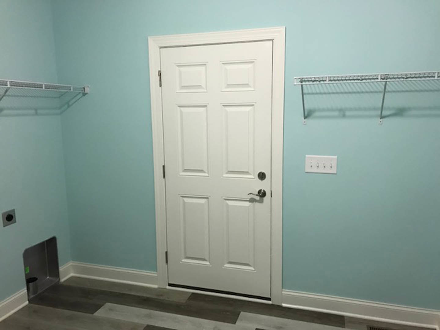 White paneled door with silver handle beside built-in white shelves, black circular wall fixture, and visible power strip on light-colored wall