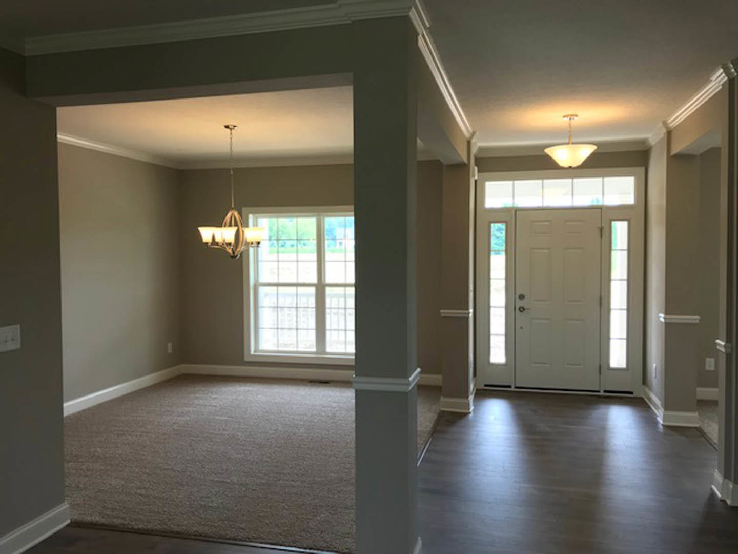 White paneled door with glass windows, wooden floor illuminated by ceiling light fixture, adjacent window with trim, neutral walls