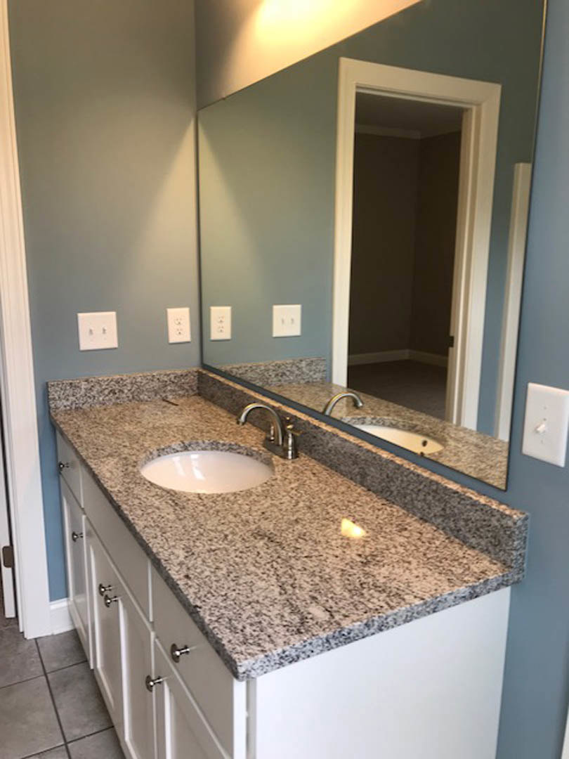 Granite bathroom countertop with undermount sink, chrome faucet, large framed mirror, white wall outlet and light switches, neutral tile backsplash