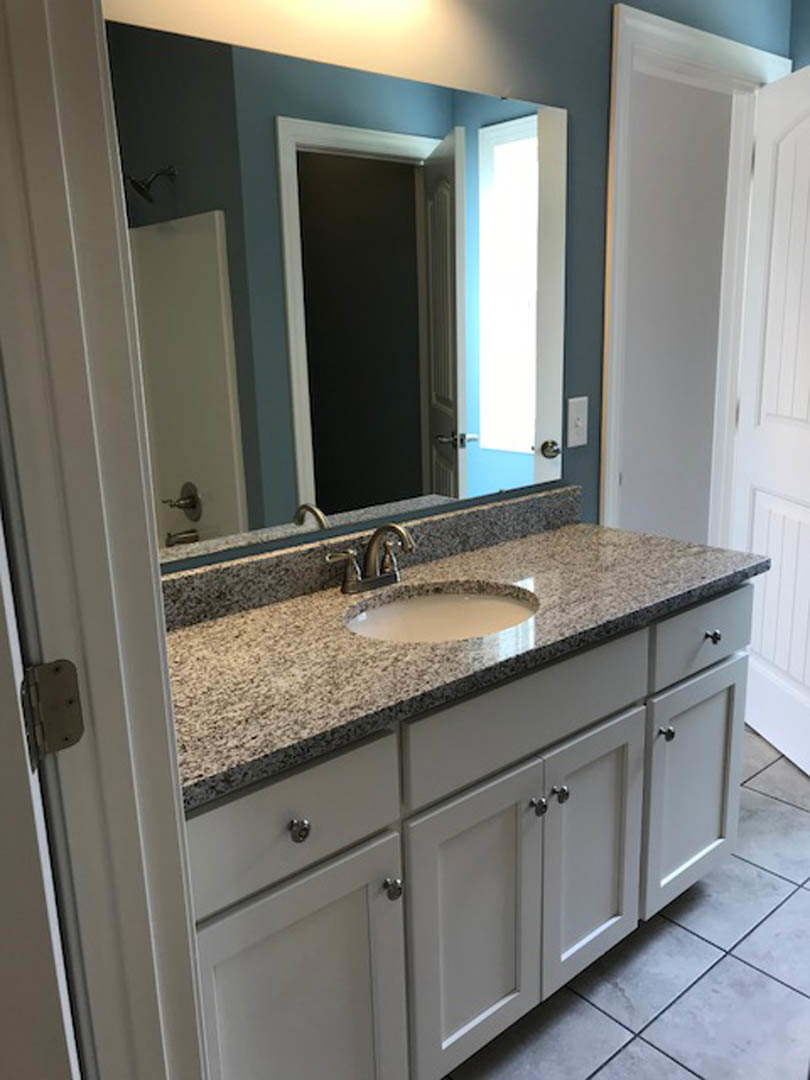 Granite countertop with undermount sink, chrome faucet, large framed mirror, tiled backsplash, white cabinetry, and paneled door in a modern bathroom