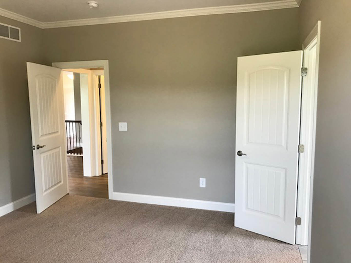 Carpeted room with two white doors featuring silver metal handles, white plaster walls, ceiling molding, and baseboards