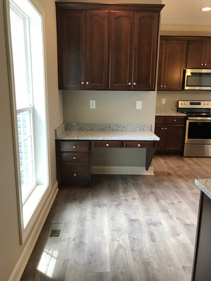 Kitchen with natural wood cabinets, granite countertops, stainless steel microwave, window above sink, wood flooring with floor vent