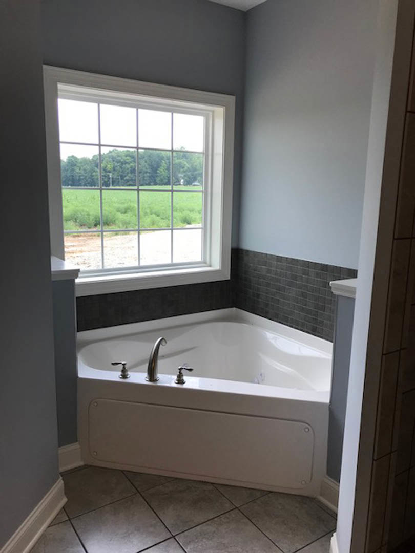 Corner bathtub with white tile surround beneath a large window, chrome faucet, and adjacent shower enclosure in a modern bathroom.