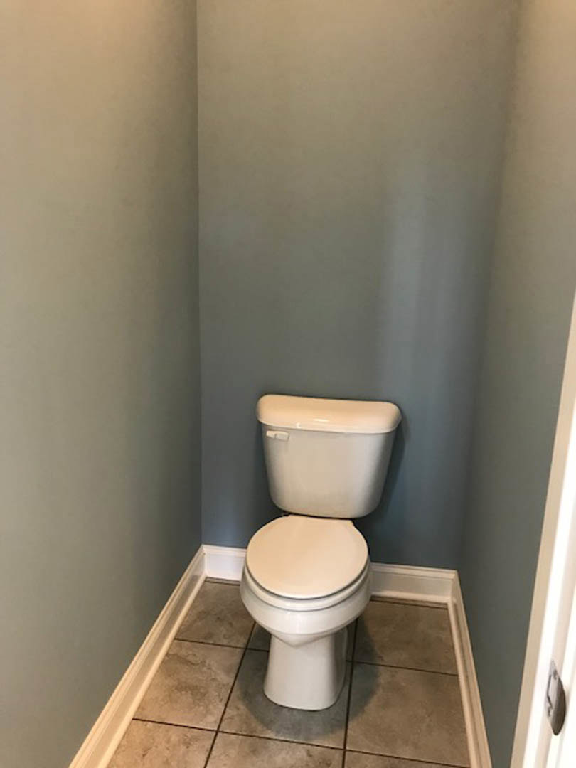 White toilet with lid up on light tile floor in compact bathroom, close to painted wall and chrome flush handle.
