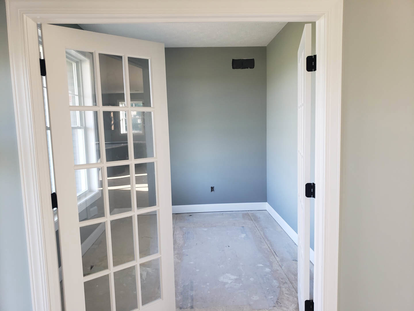 Concrete floor and white plaster walls, two white doors with glass panes, large windows, blue accent wall in a modern interior room