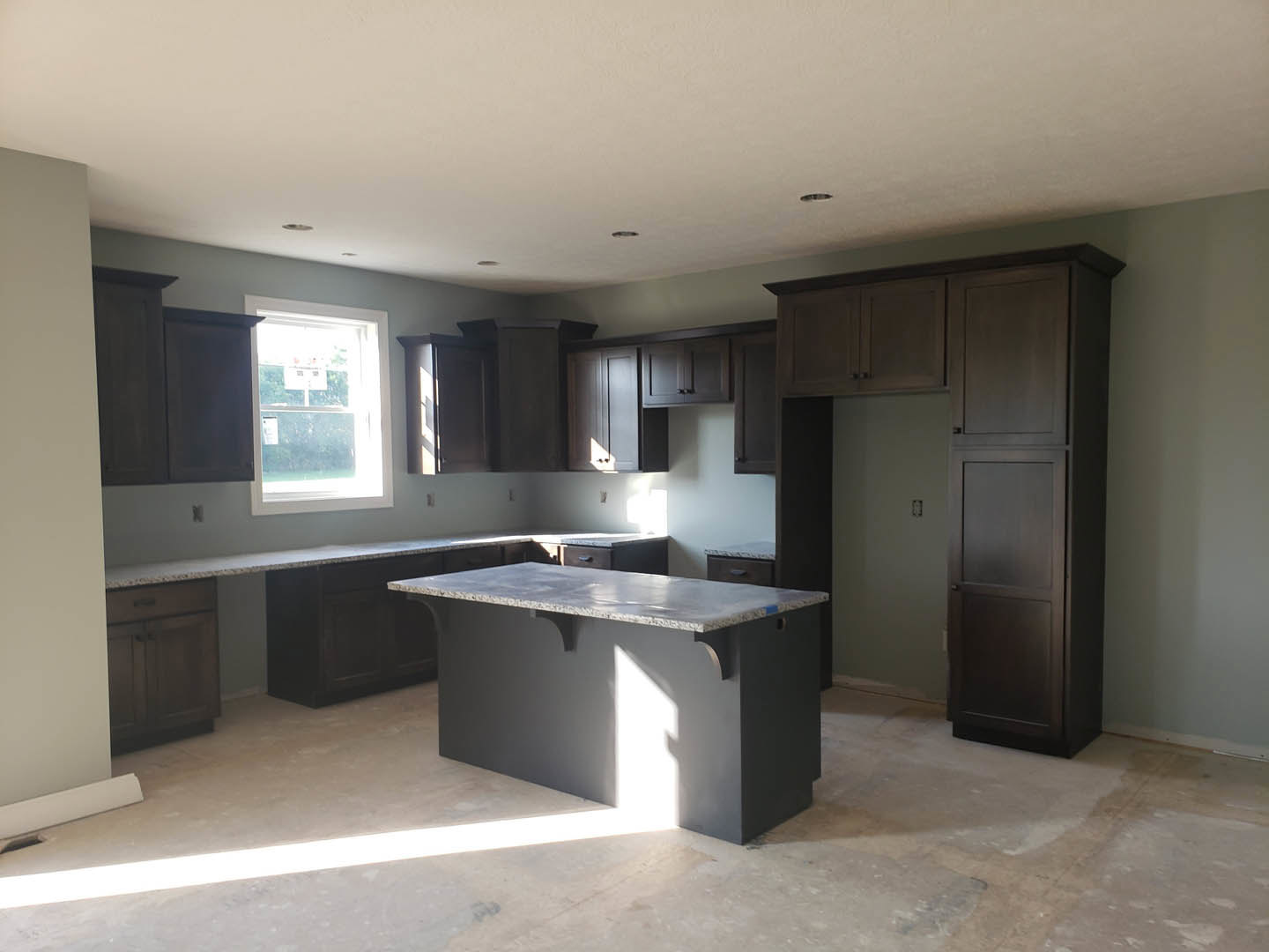 Kitchen with dark wood cabinets, light stone countertop, tile backsplash, stainless steel sink, and window with a sign.