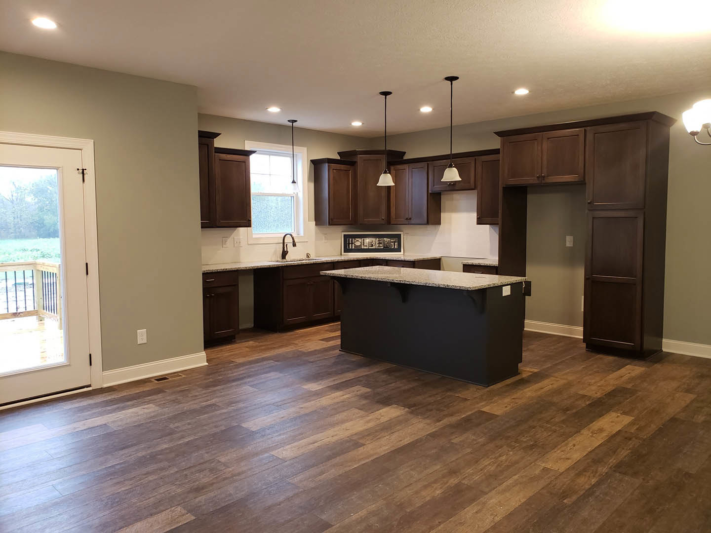 Kitchen featuring dark wood cabinets, marble-topped black counters, wood flooring, and a door opening to a balcony with natural light streaming through a window.