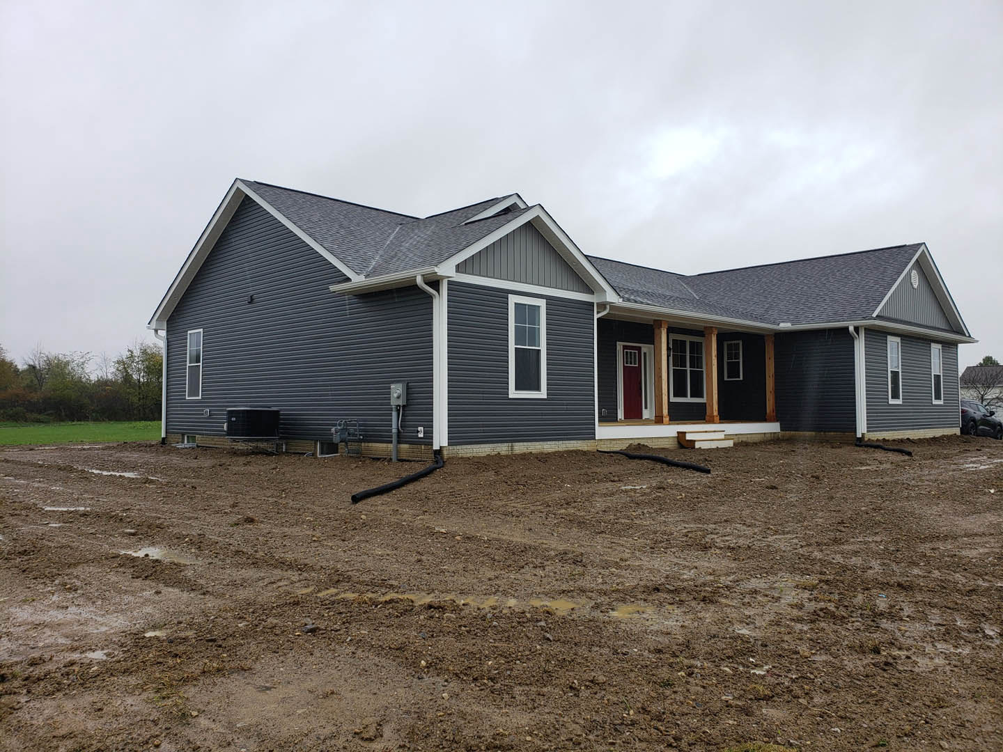 Two-story house with white siding, red front door with white trim, white-framed windows, and muddy dirt area in front yard