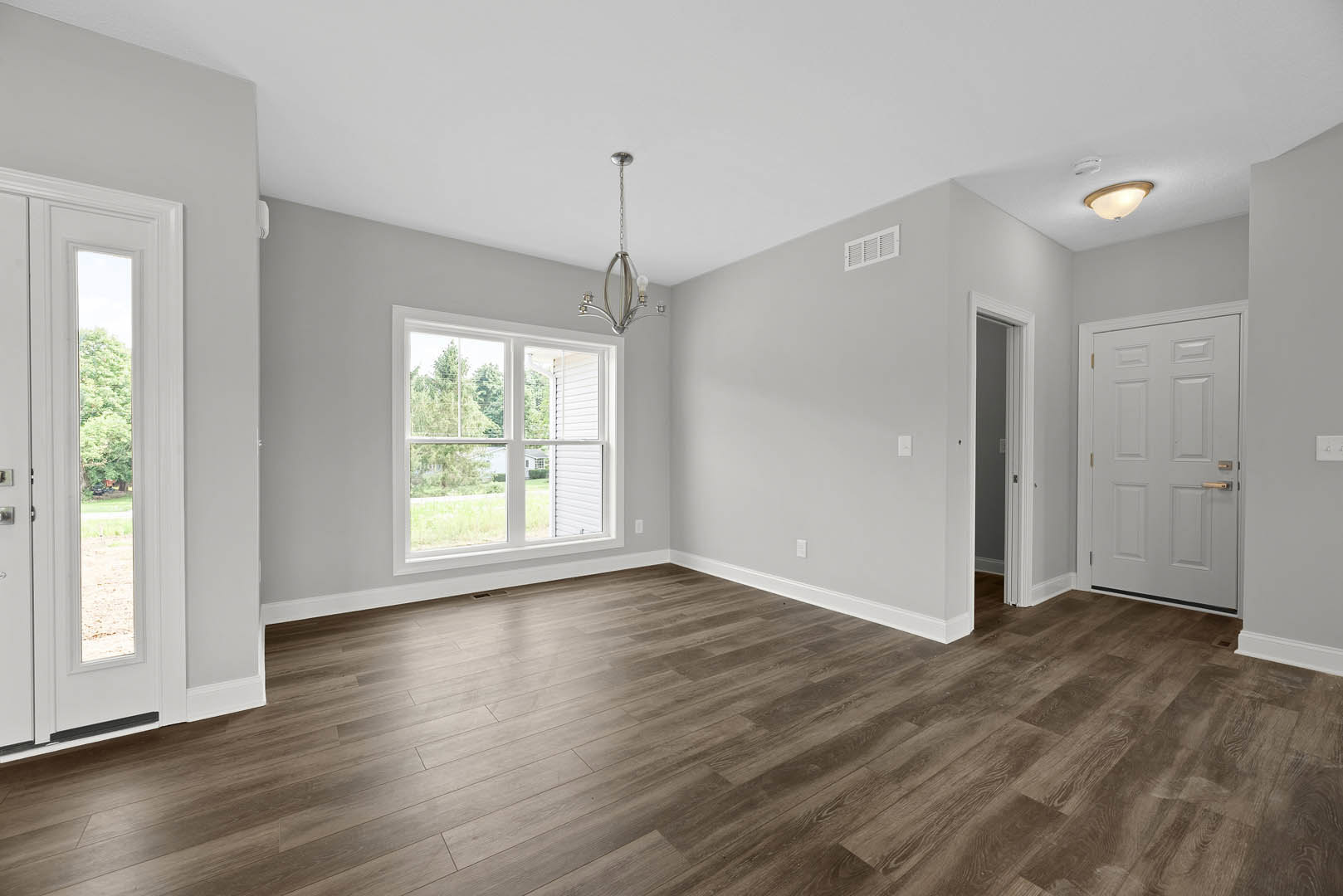 Room with hardwood floor, white door featuring gold handle and rectangular window, large window overlooking neighboring house, metal chain hanging from ceiling, plaster walls.