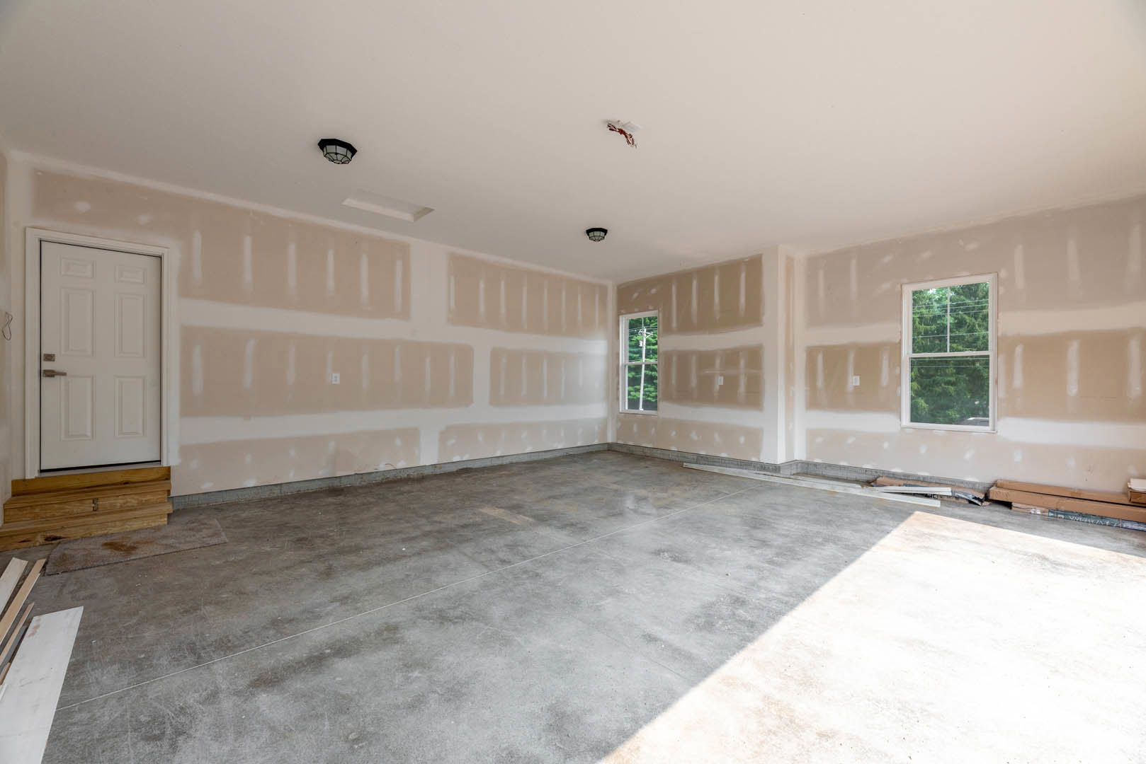 White walls and concrete floor in a minimalist room, white door with silver handle, window showing trees outside, close-up of wood surface, black-framed light fixture on ceiling