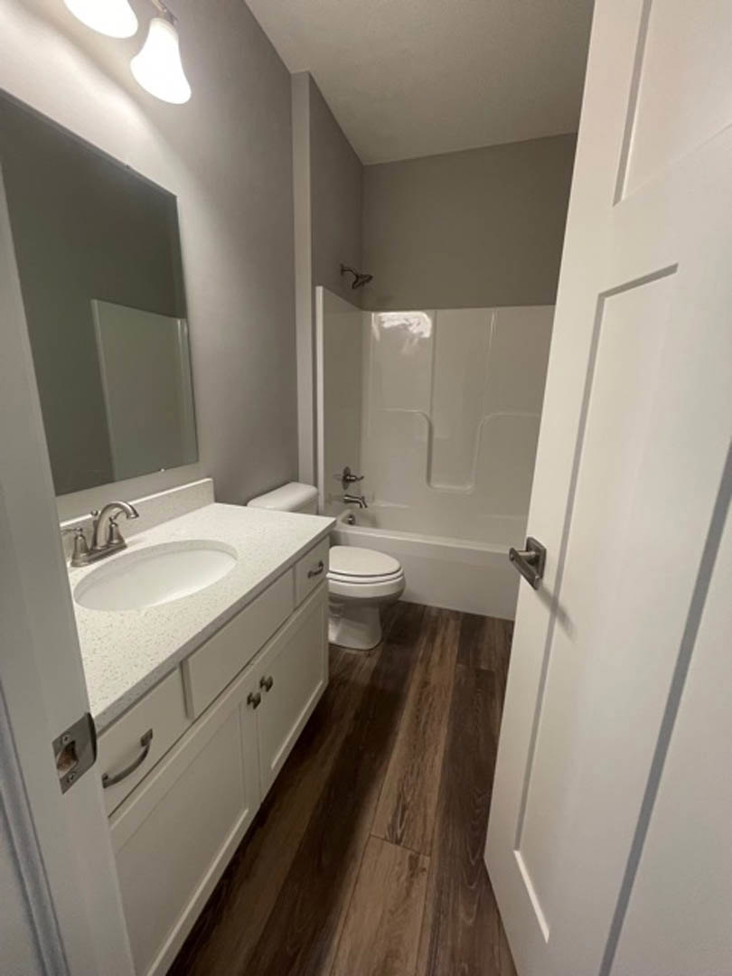 Modern bathroom with white toilet, rectangular sink on a floating vanity, large wall mirror, light gray tile flooring, and neutral tiled walls